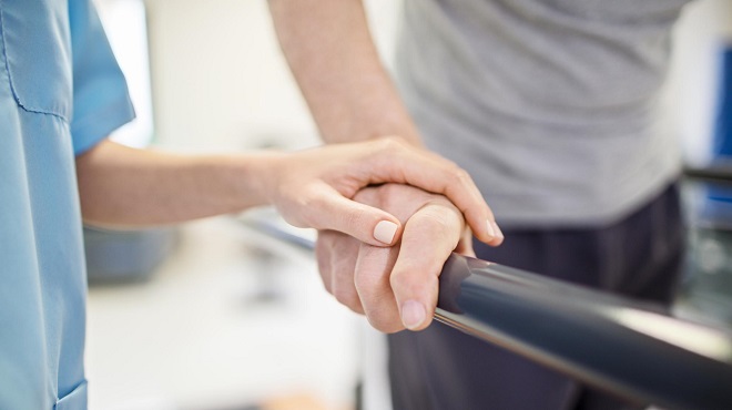 Carer's hand on a persons hand as they walk with a walking aid