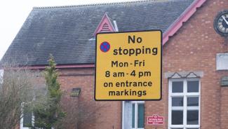 Yellow sign showing No stopping Monday to Friday from 8am to 4pm on entrance markings