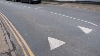 Close up of a raised section of road with 2 white arrows facing the direction of travel at the start of junction.