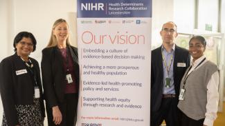 Leicestershire Health Determinants Research Collaboration representatives standing next to a poster explaining about the vision of the programme